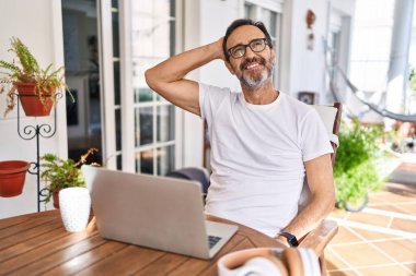 Middle age man using computer laptop at home smiling confident touching hair with hand up gesture, posing attractive and fashionable 