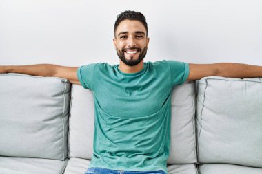 Genç Arap adam evdeki kanepede kendinden emin bir şekilde oturuyor.