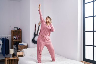 Young hispanic woman smiling confident dancing on bed at bedroom