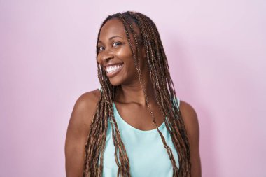African american woman standing over pink background looking away to side with smile on face, natural expression. laughing confident. 