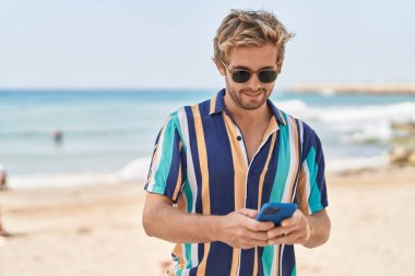 Young man tourist smiling confident using smartphone at seaside