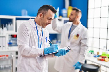 Two men scientists writing on document holding test tube at laboratory