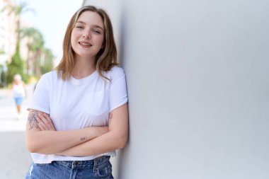 Sokakta kollarını kavuşturmuş genç beyaz bir kadın.