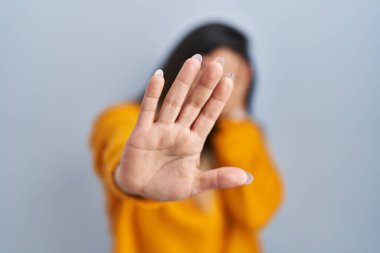 Soyutlanmış arka planda duran genç İspanyol kadın elleriyle gözlerini kapatıyor ve üzgün ve korku ifadesiyle dur hareketi yapıyor. utangaç ve olumsuz kavram. 