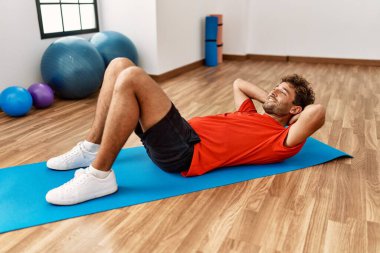 Genç İspanyol adam gülümsüyor spor merkezinde kendine güvenen karın kasları egzersizi yapıyor.