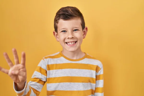 自信と幸せ笑みを浮かべている間 若い白人の子供は黄色の背景の上に立っていると指の数4を指しています — ストック写真