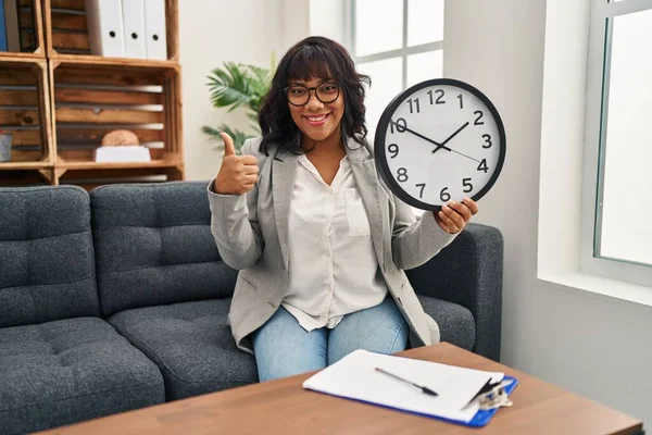 Latynoska Kobieta Pracuje Biurze Terapeutycznym Trzymając Zegar Uśmiechnięty Szczęśliwy Pozytywny — Zdjęcie stockowe