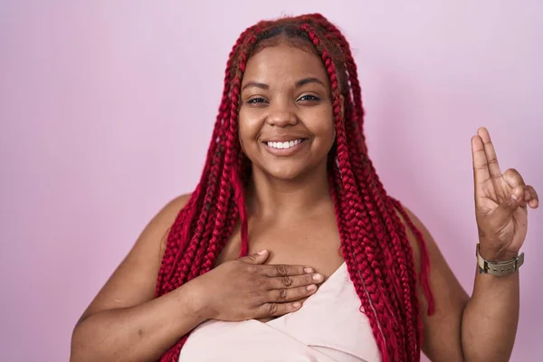 African american woman with braided hair standing over pink background smiling swearing with hand on chest and fingers up, making a loyalty promise oath