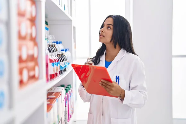 Young Hispanic Woman Pharmacist Organizing Shelving Writing Document Pharmacy — Fotografia de Stock
