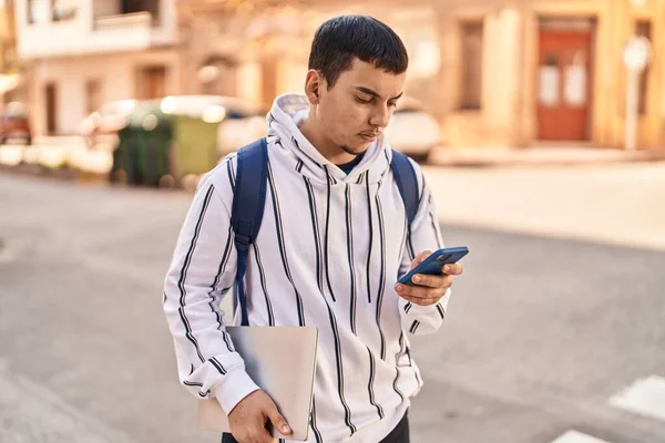 Νεαρός Φοιτητής Χρησιμοποιώντας Smartphone Κρατώντας Φορητό Υπολογιστή Στο Δρόμο — Φωτογραφία Αρχείου