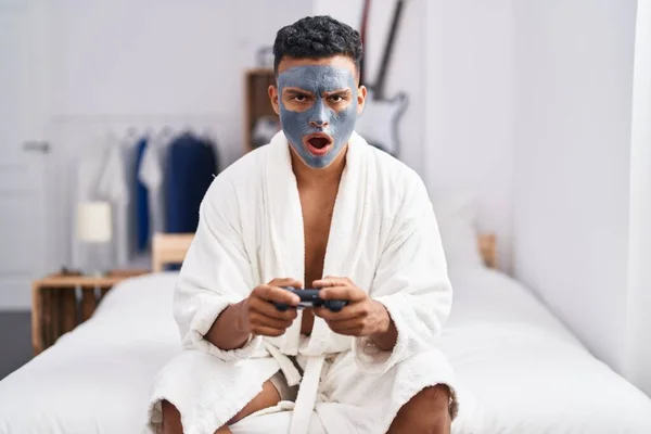 Молодой Латиноамериканец Маске Красавчика Играющий Видеоигры Шокирующим Лицом Выглядящий Скептически — стоковое фото