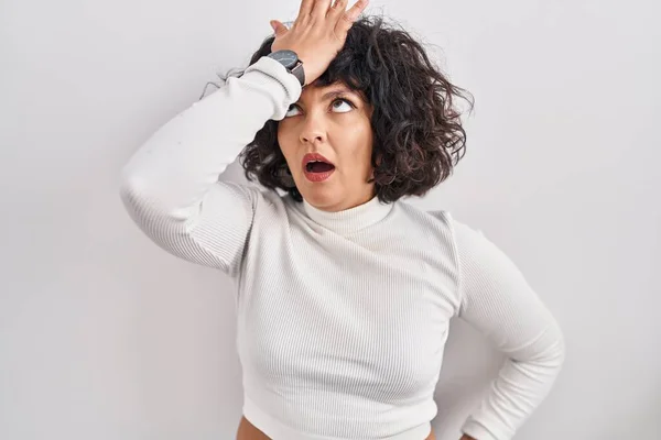 Hispanic woman with curly hair standing over isolated background surprised with hand on head for mistake, remember error. forgot, bad memory concept.