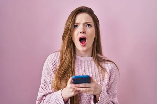 Young Caucasian Woman Using Smartphone Typing Message Angry Mad Screaming — Zdjęcie stockowe