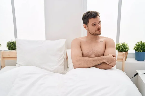 Young hispanic man unhappy sitting on bed at bedroom