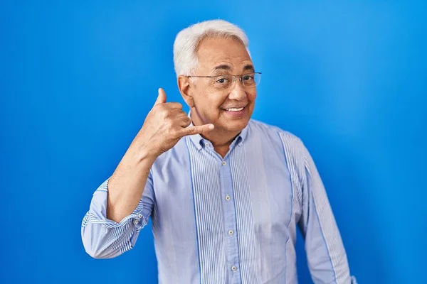 Hispanic senior man wearing glasses smiling doing phone gesture with hand and fingers like talking on the telephone. communicating concepts.