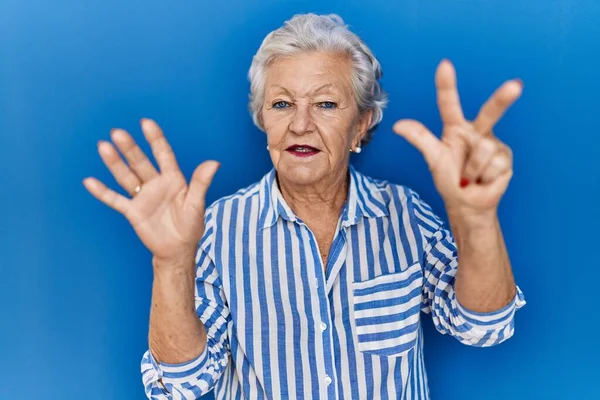 白发苍苍的老妇人站在蓝色的背景上 用八号手指指指着 面带微笑 自信而快乐 — 图库照片