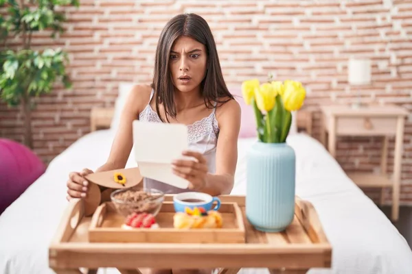 Brunette Young Woman Eating Breakfast Bed Reading Letter Shock Face — Stockfoto