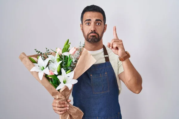 Hispanic man with beard working as florist pointing up looking sad and upset, indicating direction with fingers, unhappy and depressed.