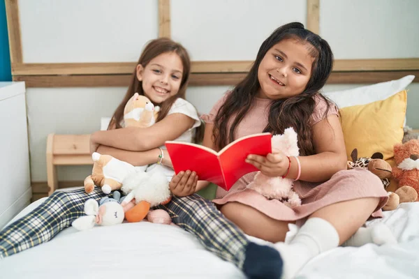 Two kids reading story book sitting on bed at bedroom