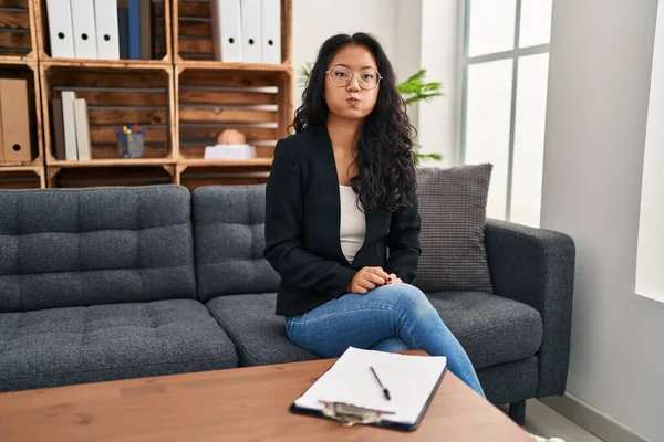 Young asian woman at consultation office puffing cheeks with funny face. mouth inflated with air, crazy expression. 