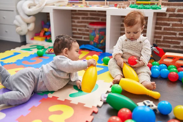 二人の可愛い赤ちゃんはボールとボウリングピンで遊んでいます床に座って幼稚園 — ストック写真