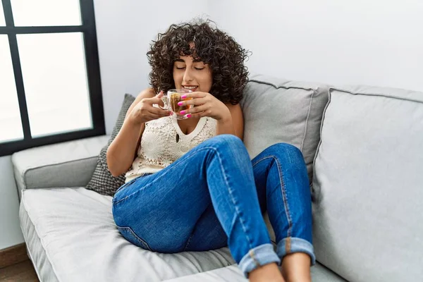 Orta Doğulu genç bir kadın gülümseyerek evde çay içiyor.