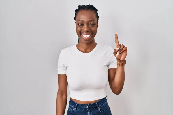 Beautiful black woman standing over isolated background showing and pointing up with finger number one while smiling confident and happy.