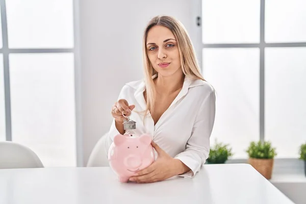 Young Blonde Woman Holding Piggy Bank House Keys Skeptic Nervous — 스톡 사진