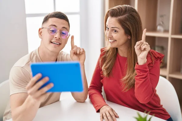 Mother and son using touchpad device smiling with an idea or question pointing finger with happy face, number one
