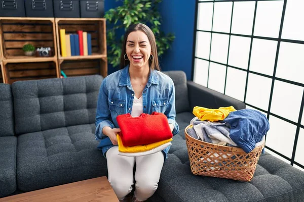 Hispanic woman holding folded laundry after ironing winking looking at the camera with sexy expression, cheerful and happy face.