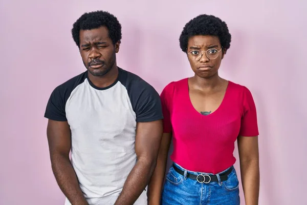 Young african american couple standing over pink background depressed and worry for distress, crying angry and afraid. sad expression.