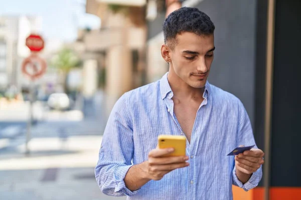 ストリートでスマートフォンやクレジットカードを使っている若いヒスパニック系の男 — ストック写真