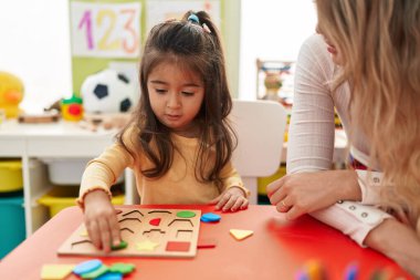 Teacher and toddler playing with maths puzzle game sitting on table at kindergarten