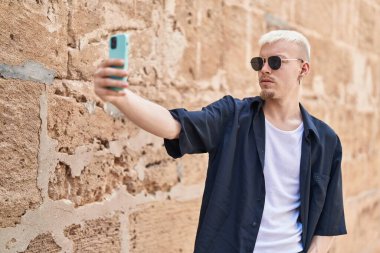 Kafkasyalı genç adam caddedeki akıllı telefonun yanında selfie çekiyor.