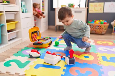 Adorable hispanic boy playing with supermarket game at kindergarten