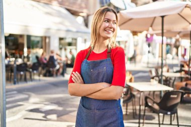 Young hispanic woman waitress standing with arms crossed gesture at coffee shop terrace