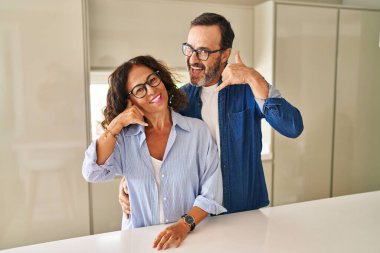 Middle age couple standing together smiling doing phone gesture with hand and fingers like talking on the telephone. communicating concepts. 
