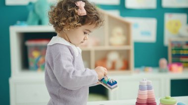 Adorable hispanic girl playing with construction blocks standing at kindergarten