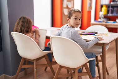 Two kids students sitting on table drawing on notebook paper at classroom