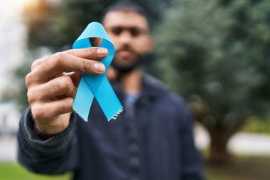 Young hispanic man holding light blue ribbon at park