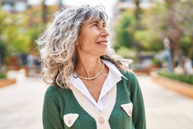 Orta yaşlı bir kadın parkta kendine güvenerek gülümsüyor.