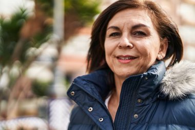 Orta yaşlı bir kadın sokakta kendine güvenerek gülümsüyor.