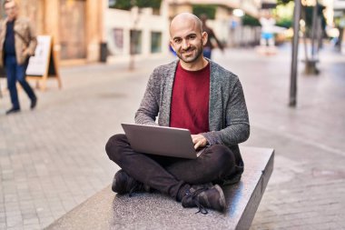 Genç adam dizüstü bilgisayar kullanıyor. Sokakta bankta oturuyor.