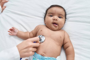 African american baby having medical examination lying on bed at bedroom