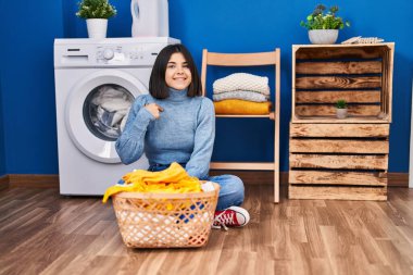 Young hispanic woman at laundry room pointing finger to one self smiling happy and proud 