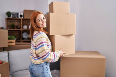 Beyaz bir kadın yeni evinde kendine güvenen bir şekilde gülümsüyor.