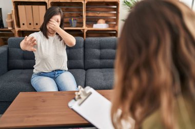 Hispanic girl with down syndrome doing therapy covering eyes with hands and doing stop gesture with sad and fear expression. embarrassed and negative concept. 