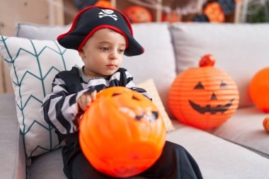 Adorable hispanic boy having halloween party holding pumpkin basket at home