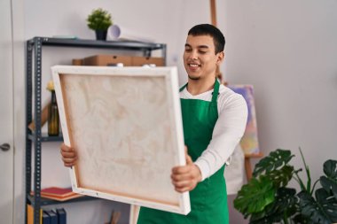 Sanat stüdyosunda kendine güvenen genç sanatçı gülümsüyor.