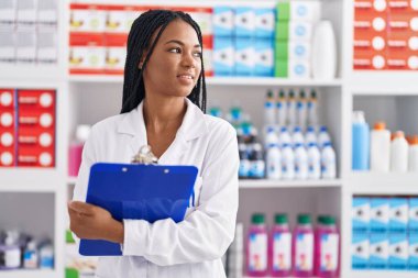 African american woman pharmacist smiling confident writing on clipboard at pharmacy